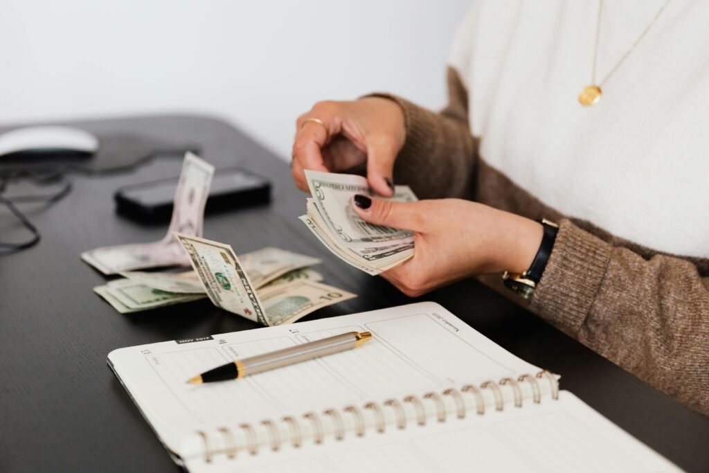 Close-up of person counting cash with notepad on desk, indicating financial tasks.