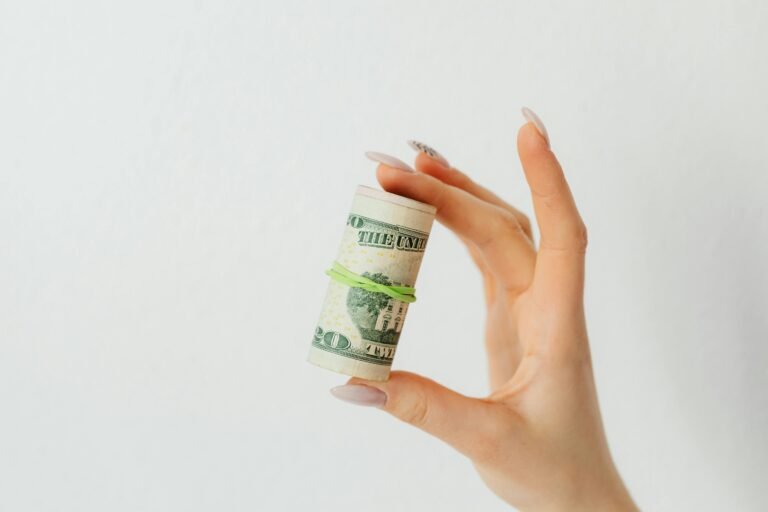 Close-up image of a hand holding a roll of US dollar bills with a rubber band.